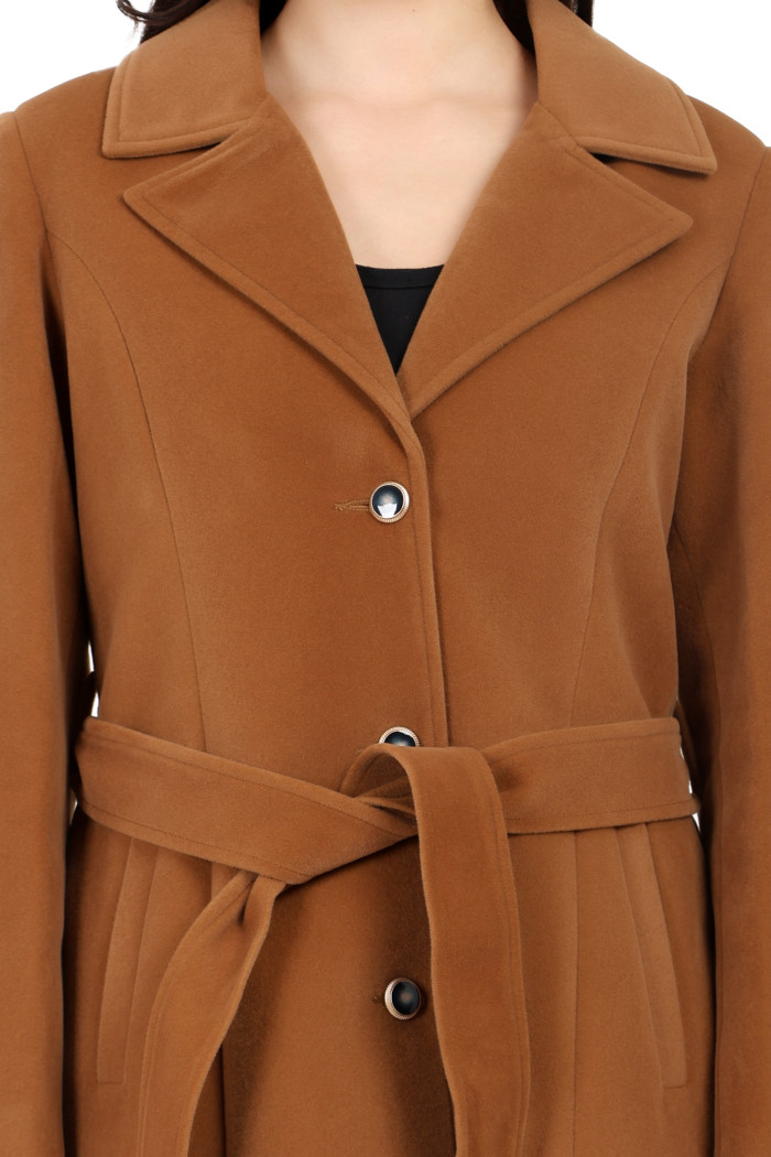 A cropped image of a woman wearing Trufit’s Long Dk. Camel Velvet coat with a lapel collar, button closure, belt and side pockets.